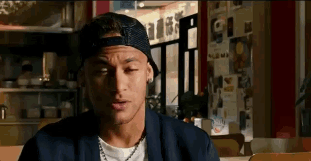 a man wearing a hat and a necklace is sitting in a restaurant .