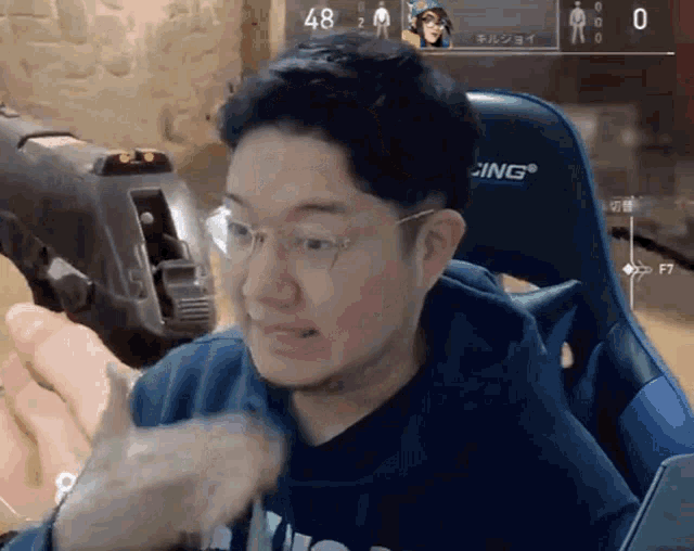 a man wearing glasses is sitting in a gaming chair with the number 48 on the screen behind him