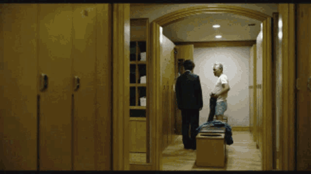 a man in a white shirt is standing in a locker room with two other men