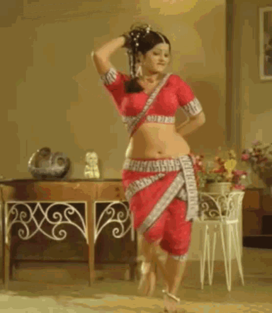 a woman in a red crop top and pants is dancing in a living room .