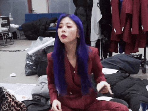 a woman with purple hair is sitting on the floor in a room with clothes and a chair that has the number 5 on it
