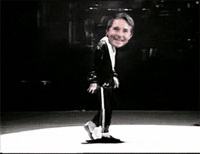 a man in a black suit is dancing on a white stage
