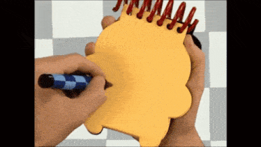 a person is writing on a yellow notebook with a blue and white marker