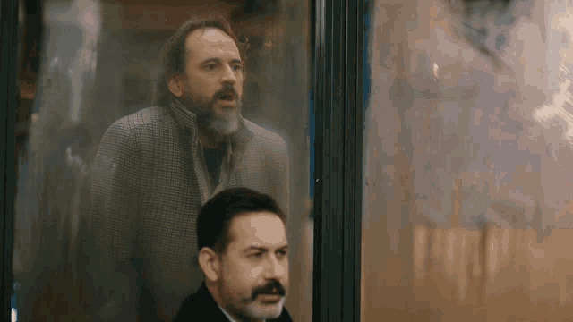 a man with a beard and mustache is looking out a window