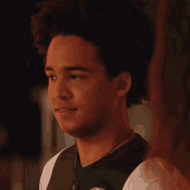 a young man with curly hair is wearing a white shirt and a green vest