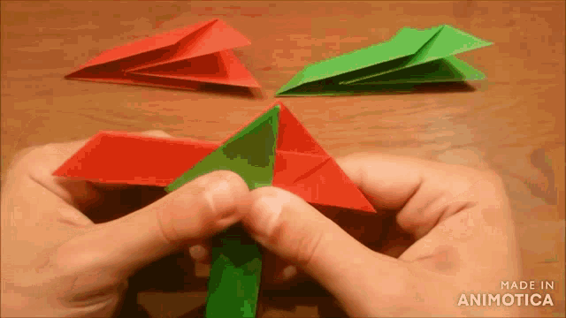 a person is holding a red and green origami object with the words made in animotica on the bottom