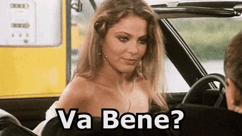 a woman is sitting in a car talking to a man and the words va bene are on the screen