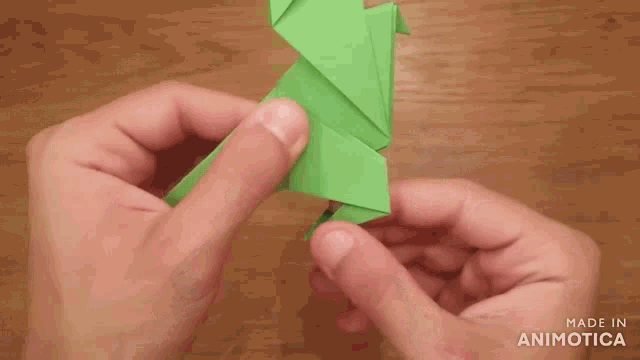 a person is holding a green origami bird in their hands with the words made in animotica below them