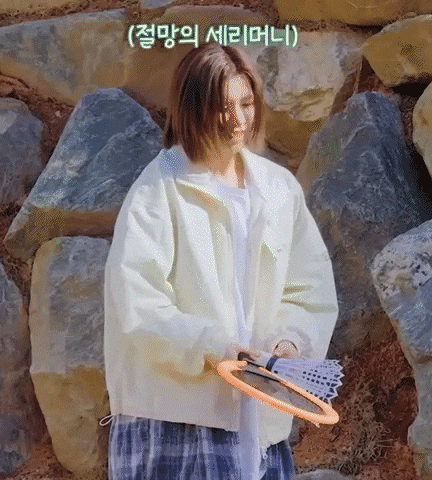 a woman in a white jacket is standing in front of a rock wall holding a badminton racket .