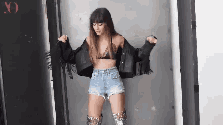 a woman in a bra and denim shorts is dancing in a room .