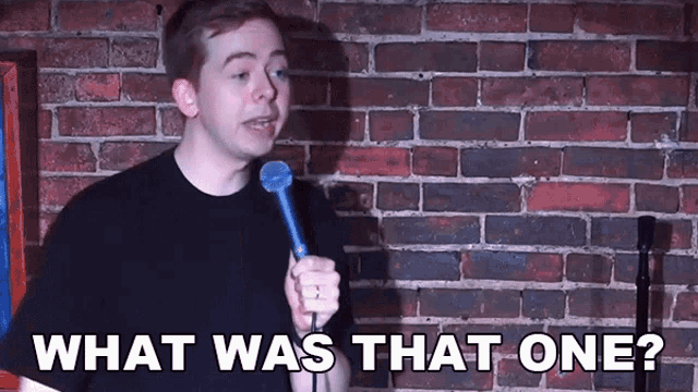a man holding a microphone in front of a brick wall with the words what was that one