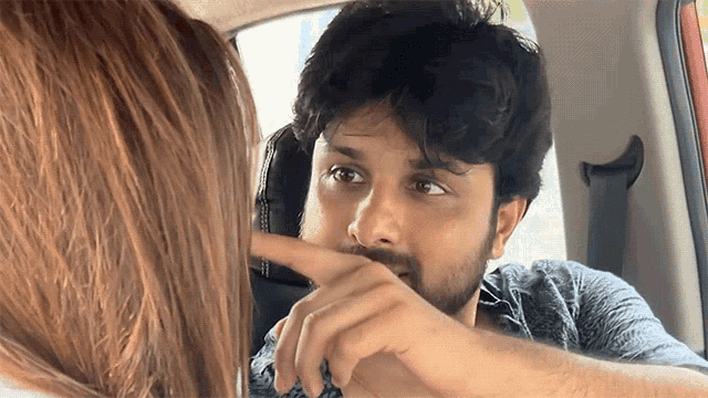 a man with a beard is pointing at a woman in a car