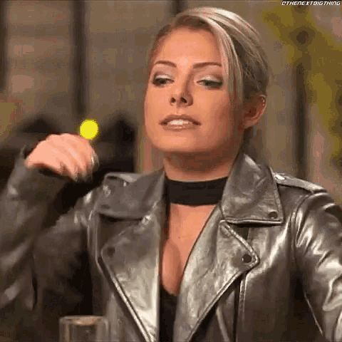 a woman in a leather jacket and choker is sitting at a table with a glass of wine .