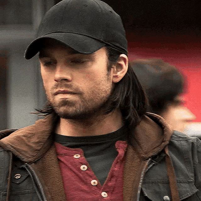 a man with long hair wearing a black hat and a brown jacket