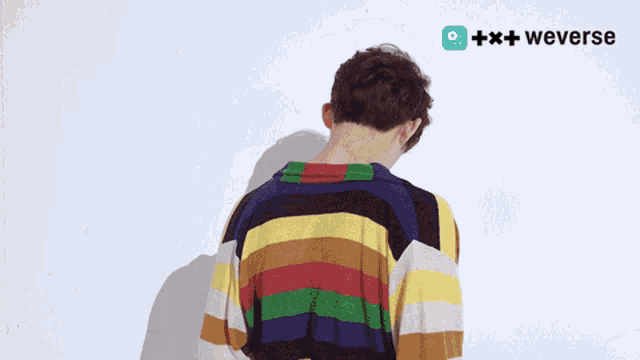 a person wearing a colorful striped shirt is standing in front of a white wall with a weverse logo