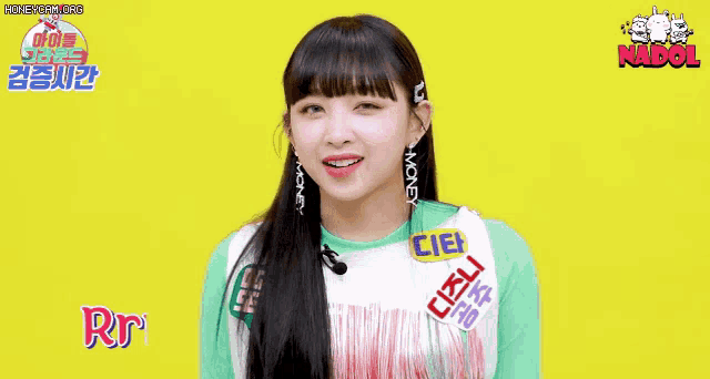 a girl with long black hair is wearing a green shirt and earrings and smiling .