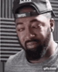 a man with a beard wearing a hat and ear buds is looking down .