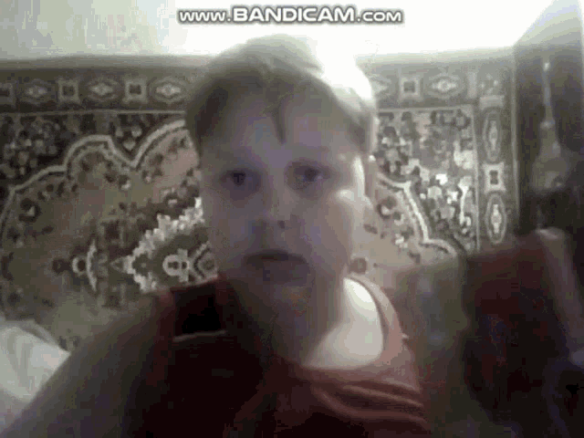 a young boy in a red tank top is looking at the camera .