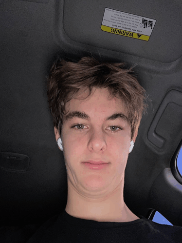 a young man is sitting in a car with a warning sign on the sun visor