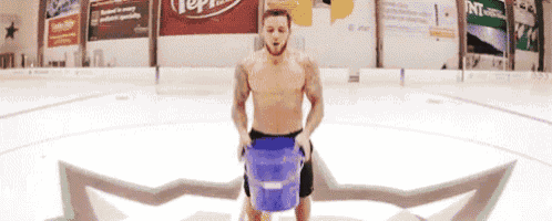 a shirtless man is carrying a blue bucket on a ice rink in front of an advertisement for pepsi