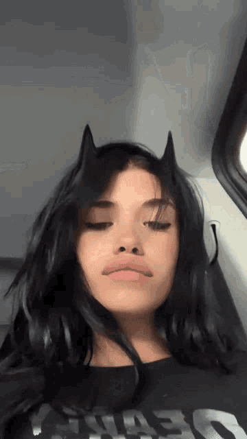 a woman with black hair and devil horns on her head is sitting in a car .