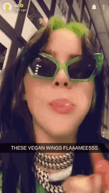 billie eilish wearing green sunglasses and a green headband says these vegan wings flaaameesss