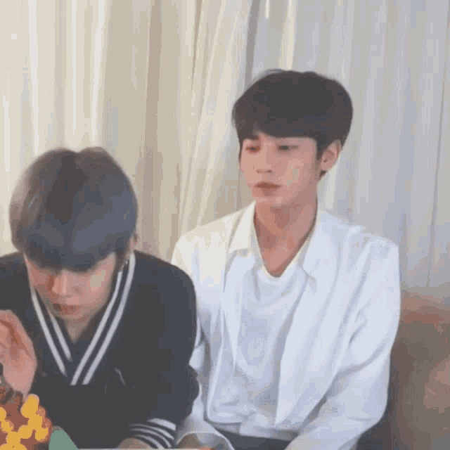 two young men are sitting on a couch and one is wearing a white shirt