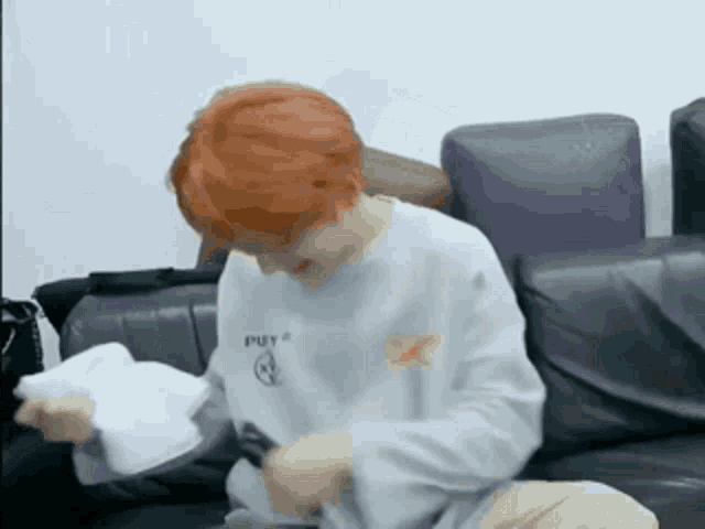 a boy with red hair is sitting on a couch holding a piece of paper .
