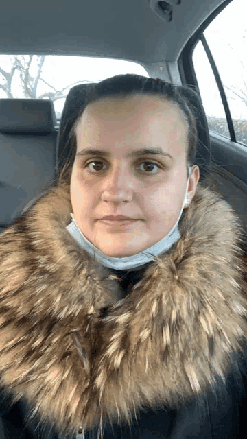 a woman wearing a mask and a fur collar is in a car