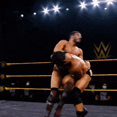two men are wrestling in a ring and one of them is laying on the ground .