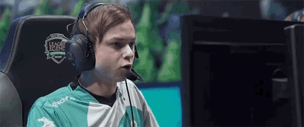 a man wearing headphones and a league of legends shirt is sitting in front of a computer monitor .