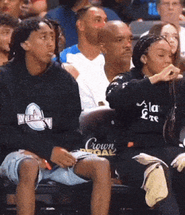 a man wearing a black crown regal sweatshirt sits in the stands