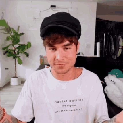 a man wearing a hat and a white t-shirt is sitting in a room .