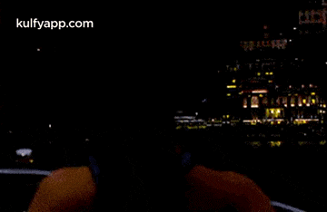 a person is driving a car at night with a city in the background and the website kulfyapp.com is visible .