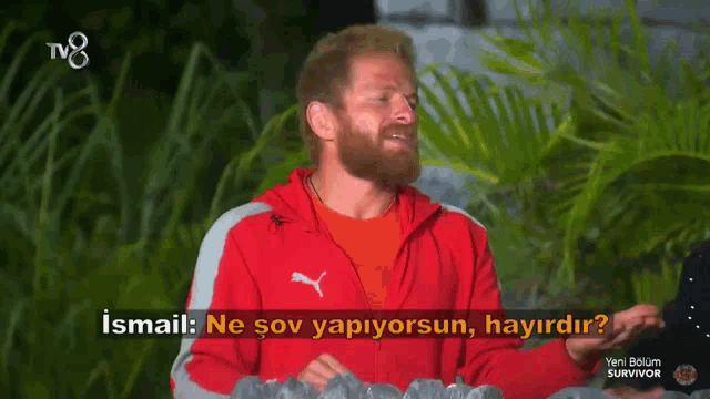 a man in a red puma jacket is talking on a tv show