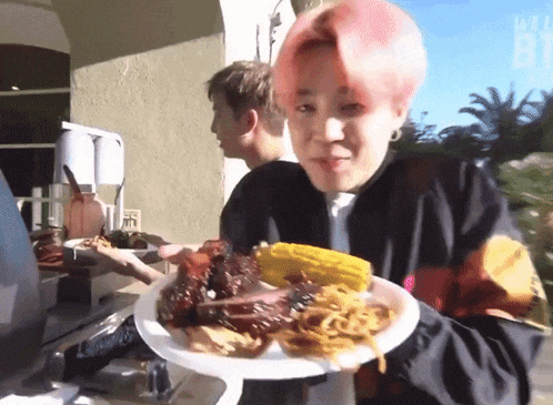 a young man with pink hair is holding a plate of food with meat and corn on the cob .
