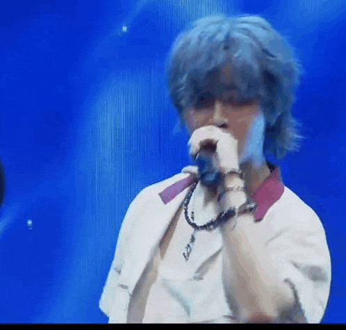a man with blue hair is singing into a microphone on a blue background .