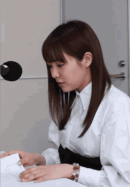 a woman in a white shirt is sitting at a desk with a microphone in front of her