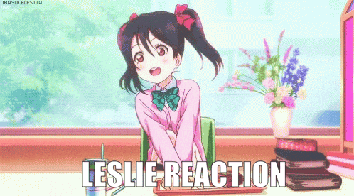 a girl in a pink shirt is sitting at a desk with the words leslie reaction above her
