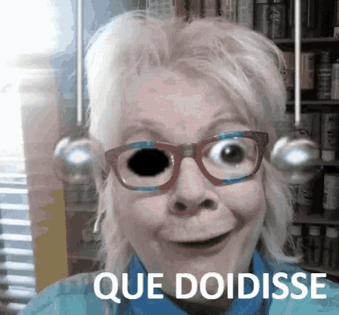 a woman wearing glasses says que doidisse in front of a book shelf