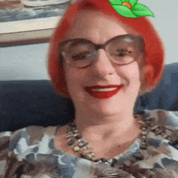 a woman with red hair and glasses is smiling and wearing a necklace .
