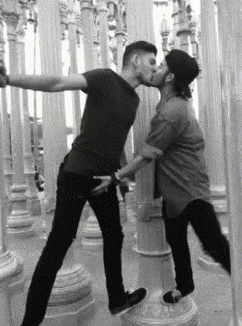 two men kissing in front of a row of pillars