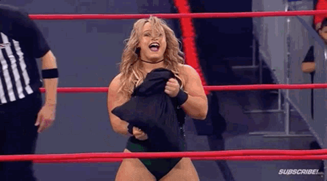 a woman in a bikini is standing in a wrestling ring holding a black shirt .