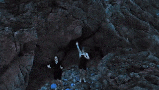 a man and a woman are standing in a cave with their hands in the air