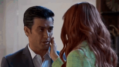 a woman is touching a man 's face while they are looking at each other .