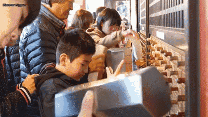a group of people are standing in a line looking at a machine with a hammer .