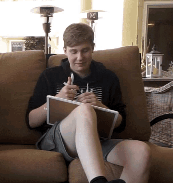 a young man sits on a couch with a tablet and a pen in his hand