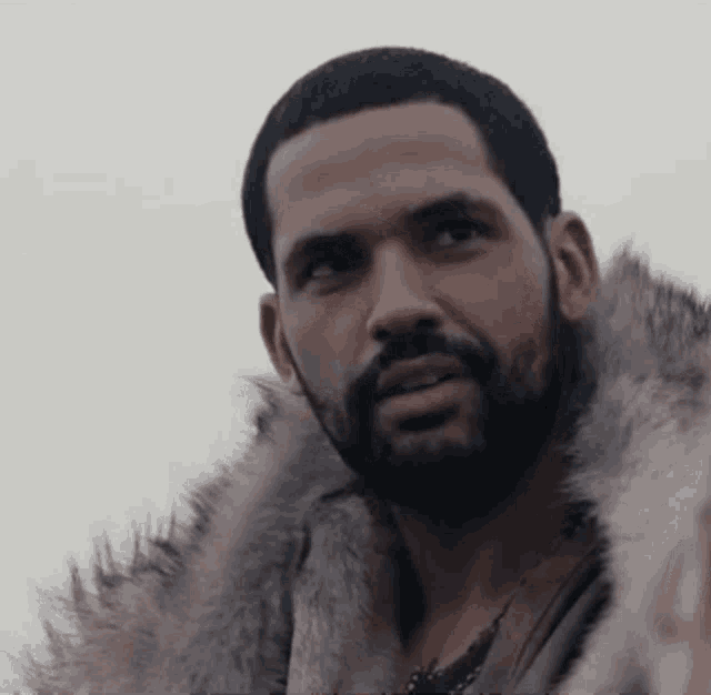 a man with a beard wearing a fur coat is looking at the camera .