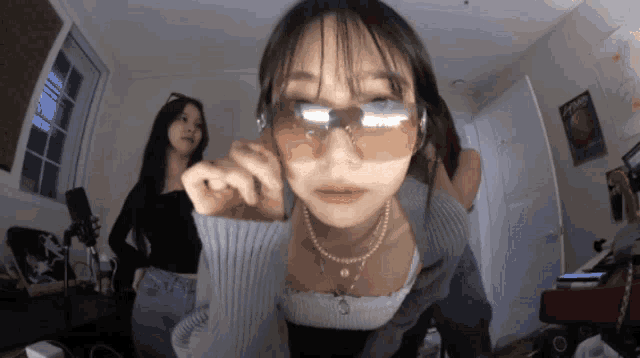 a woman wearing sunglasses and a pearl necklace looks at the camera in a room