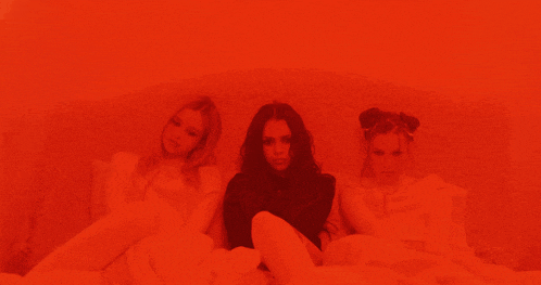 three women are sitting on a bed in a red light